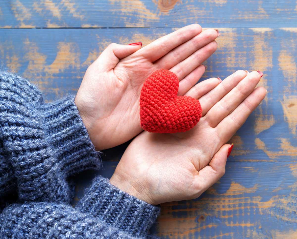 Female hands holding handmad knitted red heart